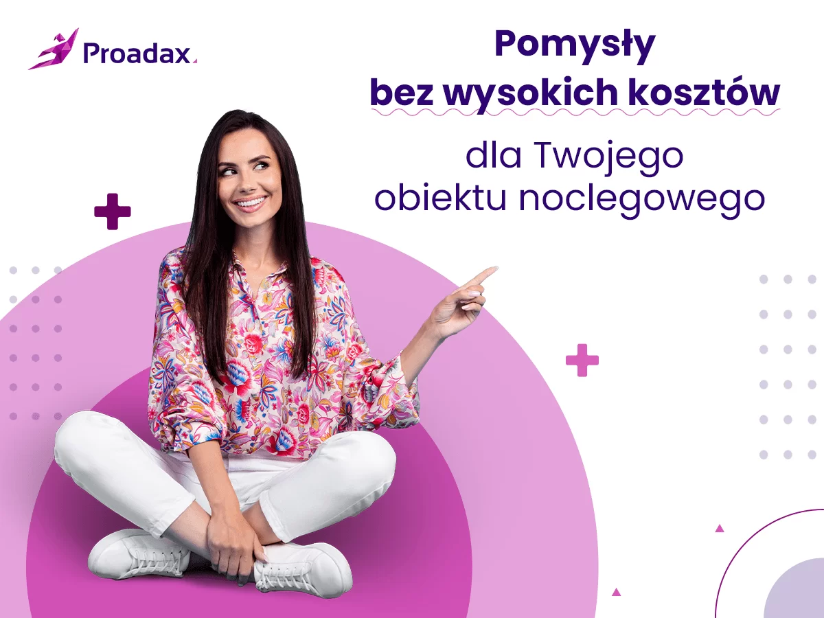 Kobieta w kwiecistej bluzce i białych spodniach siedzi na podłodze z nogami skrzyżowanymi i uśmiecha się, wskazując w górę. W tle znajduje się logo Proadax i napis "Pomysły bez wysokich kosztów dla Twojego obiektu noclegowego